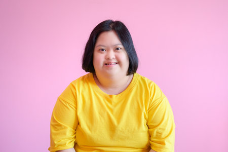 Image of young Asian woman with Down syndrome smile She is a cerebral palsy student wearing a yellow dress on a pink background.の写真素材