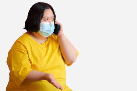 Image of a handicapped woman with Down Syndrome learning with a mobile phone making gestures on the phone She is a disabled student with Down syndrome wearing a medical mask on the pink background.の写真素材
