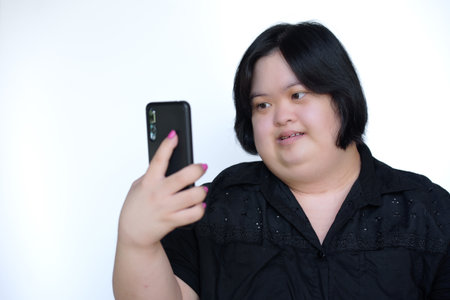 Close-up portrait of a fat Asian woman. with disabilities or children with Down syndrome Playing on the phone and smiling happily on white background. Concept: Down syndrome.の写真素材