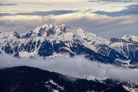 Beautiful winter mountain landscape with snow covered peaks and clouds at sunsetの写真素材
