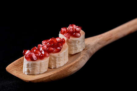 pomegranate seeds with banana on a wooden spatula on a dark background. vegetarian version of caviar sandwichの写真素材