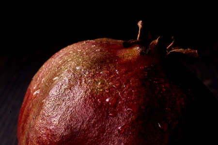 ripe pomegranate on a dark background shiny from water drops falling on it