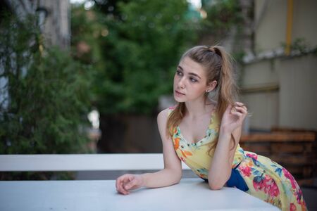 a young girl with long white curls in a dress walks through the old town in the summer. girl in a flowers dress with light curls. Beautiful blonde woman walking in yellow dress. Fashion summer photo.の写真素材