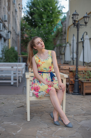 a young girl with long white curls in a dress walks through the old town in the summer. girl in a flowers dress with light curls. Beautiful blonde woman walking in yellow dress. Fashion summer photo.の写真素材