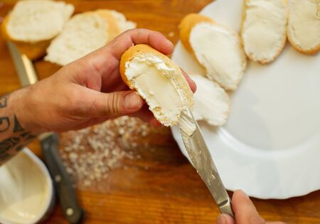 The cook spreads the cottage cheese on the bread. Men's hands spreading soft cheese on a French loaf