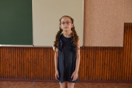 Cheerful little schoolgirl standing at the blackboard.Schoolgirl with two pigtails in glasses. Seriously disposed student. Modern children. A girl of 9 years old. 4th grade school.の写真素材