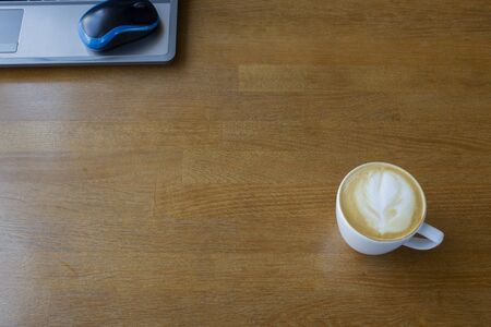 Workspace with laptop, a cup of coffee and a mouse for a laptop, phone, glasses on a white wooden table. Gray laptop, blue mouse for working at a computer, blue glasses for vision, cappuccino.の写真素材