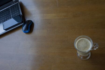 Workspace with laptop, a cup of coffee and a mouse for a laptop, phone, glasses on a white wooden table. Gray laptop, blue mouse for working at a computer, blue glasses for vision, cappuccino.の写真素材
