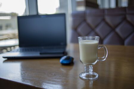 Workspace with laptop, a cup of coffee and a mouse for a laptop, phone, glasses on a white wooden table. Gray laptop, blue mouse for working at a computer, blue glasses for vision, cappuccino.の写真素材