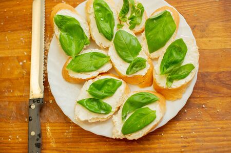 Cook smears cottage cheese on bread. Male hands spread soft cheese on french bread and spread basil. Vegetarian sandwiches. Healthy food. Healthy lifestyle. Summer foodの写真素材