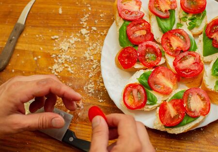 The cook spreads the cottage cheese on the bread with tomato. Men's hands spreading soft cheese on a French loaf. Vegetarian sandwiches on a wooden board. Healthy food. Seasonal food.の写真素材
