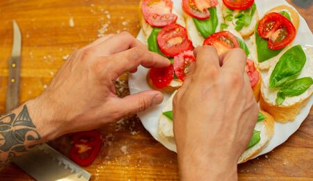 The cook spreads the cottage cheese on the bread with tomato. Men's hands spreading soft cheese on a French loaf. Vegetarian sandwiches on a wooden board. Healthy food. Seasonal food.の写真素材