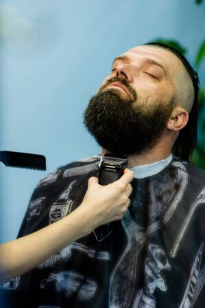 Hipster client visiting barber shop. Mens fashion. Bearded man after barber shop. Man hipster having barber shave barbershop hair machine. fashionable haircut, rear view. Work in a beauty salon.の写真素材