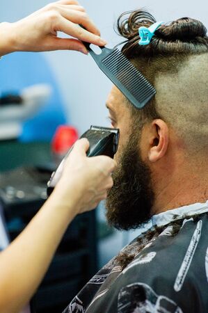 Hipster client visiting barber shop. Mens fashion. Bearded man after barber shop. Man hipster having barber shave barbershop hair machine. fashionable haircut, rear view. Work in a beauty salon.の写真素材