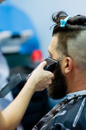 Hipster client visiting barber shop. Mens fashion. Bearded man after barber shop. Man hipster having barber shave barbershop hair machine. fashionable haircut, rear view. Work in a beauty salon.の写真素材