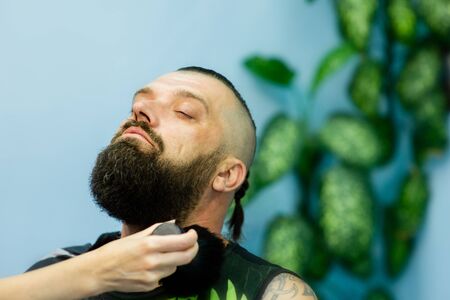 Hipster client visiting barber shop. Mens fashion. Bearded man after barber shop. Man hipster having barber shave barbershop hair machine. fashionable haircut, rear view. Weave braids.の写真素材