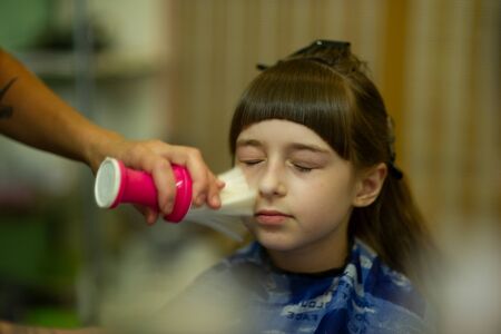 Hairdresser making a hair style to cute little girl. The girl cuts off the bangs. Work hairdresser. Change the image. Change hairstyle. Fashionable baby. A series of photos of haircuts baby bangs.の写真素材