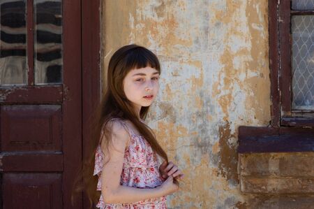 Adorable happy little girl outdoors. Portrait of caucasian kid enjoy summer. A girl of 9 years old in a dress in a flower. Beautiful haircut with bangs from the girl. Long hair of light brown color.の写真素材