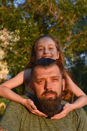 Family time. Little girl hugging her dad with a beard. Summer walk. Child girl with blond hair rejoices with a parent. The most valuable time is the time spent with your beloved family. Childhoodの写真素材