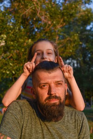 Family time. Little girl hugging her dad with a beard. Summer walk. Child girl with blond hair rejoices with a parent. The most valuable time is the time spent with your beloved family. Childhoodの写真素材