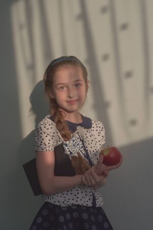 A girl with a pigtail and blond hair of 9 years old. Cute schoolgirl with red Apple in hand.A child with a book. School uniform. Educational concept. School concept. Back to Schoolの写真素材
