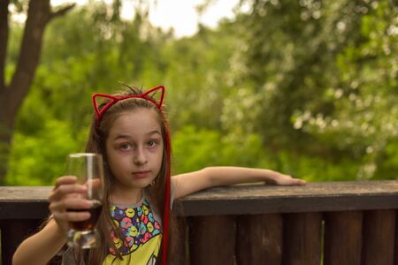 The girl wore a hoop cat ears and a red strand. A child walks in a cafe and drinks a drink from a glass. 9-year-old girl Modern children. Summer terrace. sunny day. Modern children.の写真素材