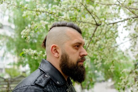 A man in a leather jacket with a brunette beard. brutal man brunette with beard on her face. street...