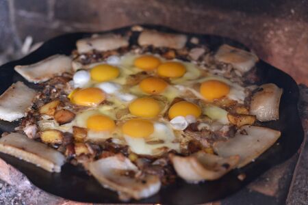 Eggs are fried on a fire in the street. Fried eggs with bacon. A dish of many fried eggs on a bonfire in the oven. Grain fat. Street food. Rest with food. Grilled eggs in a panの写真素材