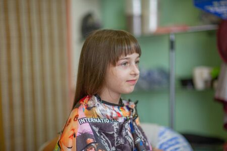 Stylist hairdresser makes a hairstyle for a cute little girl in a beauty salon.Hairdressing, hair cutting.A girl is given the length of her hair in a beauty salon.A series of photos is a haircutの写真素材