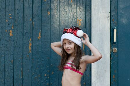 Little girl in santa claus hat on blue background.A little girl is having fun and playing in christmas eve at Santa Claus hat, in a bathing suit, a background of blue.concept of christmas and holidaysの写真素材