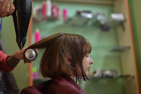 Stylist hairdresser makes a hairstyle for a cute little girl in a beauty salon.Hairdressing, hair cutting.A girl is given the length of her hair in a beauty salon.A series of photos is a haircutの写真素材
