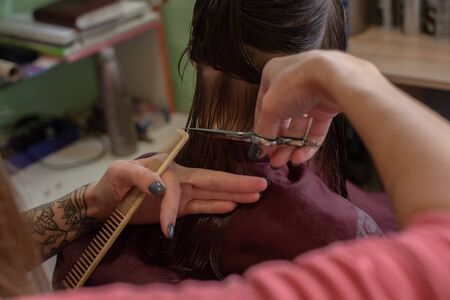 Stylist hairdresser makes a hairstyle for a cute little girl in a beauty salon.Hairdressing, hair cutting.A girl is given the length of her hair in a beauty salon.A series of photos is a haircutの写真素材