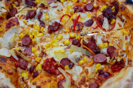 Fresh pizza.Pizza with cheese and sausages.Tasty pizza with sauce.Pizza in a white plate on a white table in a pizzeria or Italian restaurant in daylight.Pizza with chicken, hunting sausages and baconの写真素材