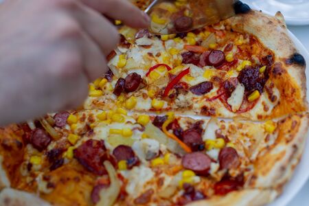 Fresh pizza.Pizza with cheese and sausages.Tasty pizza with sauce.Pizza in a white plate on a white table in a pizzeria or Italian restaurant in daylight.Pizza with chicken, hunting sausages and baconの写真素材