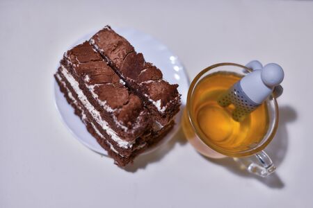 simple tea cup. Green tea in a transparent cup. A cup of herbal or green tea with a teapot strainer man in it. tea on a white surface. Healthy drink. Food. A cup of tea with cake. Chocolate cakeの写真素材