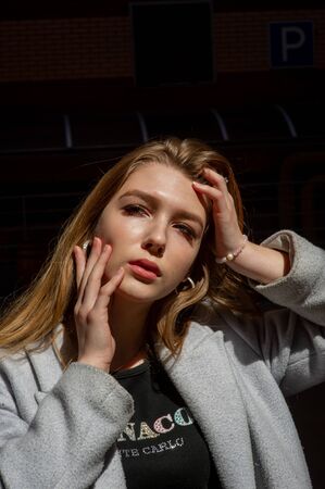Stylish young pretty girl in a gray coat looks at the camera and smiles slightly against the...