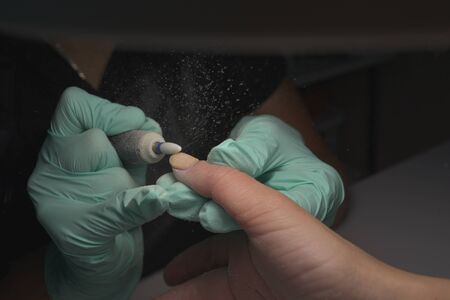 Woman hands receiving a manicure in beauty salon. Nail filing. Close up, selective focus.Female hands in the process of manicure, cutting of the cuticle, correction of the shape of the nail plateの写真素材