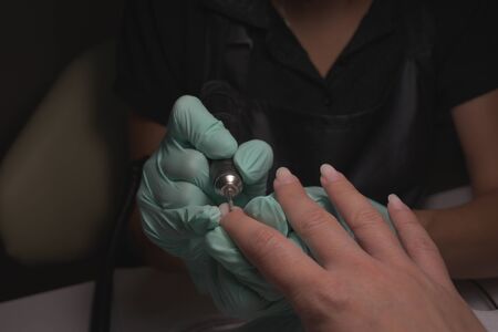 Woman hands receiving a manicure in beauty salon. Nail filing. Close up, selective focus.Female hands in the process of manicure, cutting of the cuticle, correction of the shape of the nail plateの写真素材