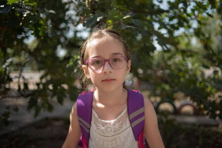 Schoolgirl with a violet rucksack and purple glasses. Girl in a white dress, wearing glasses in...