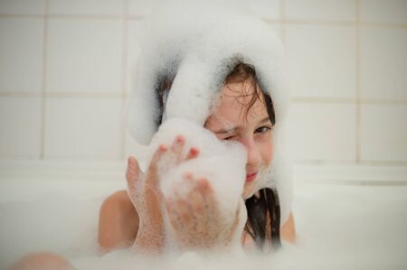 Young girl inside the bath. A little girl bathes in a bathtub with foam. A girl of 9 years old takes a bath. Purity conceptの写真素材