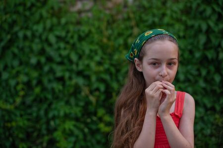 Little girl on the street against a background of green foliage. Girl with long hair. Child 9-10...