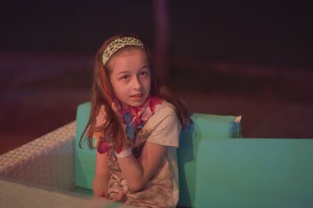 Young European teenage brunette curly model posing.Teenager girl. Girl 10 years old posing on the veranda in a cafe. A child on the background of the city.Girl 9 years old at a party in a summer cafeの写真素材
