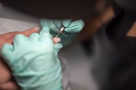 A manicure hand with a nail lies on a manicure hand in blue hygienic gloves.Hands on the manicure of...