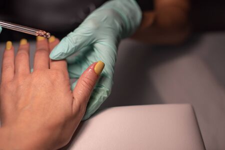 A manicure hand with a nail lies on a manicure hand in blue hygienic gloves.Hands on the manicure of the master.A woman doing a manicure,cut the cuticle.Well-groomed hands.Hygienic manicure.の写真素材