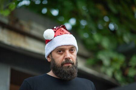 Santa Claus walking on city street. Man with a beard on the street in the summer in a hat of Santa...
