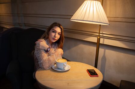 young pretty woman in cafe. Girl in a cafe in a beige blouse. Young girl in a coffee shop in black...