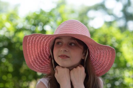 portrait of pretty cheerful woman wearing white dress and straw pink hat in sunny warm weather...