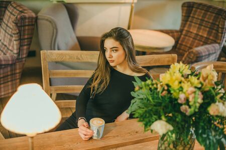 Beautiful elegant brunette girl wearing a black dress is relaxing in a street cafe....
