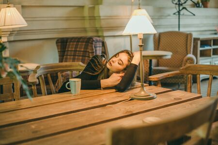 Beautiful elegant brunette girl wearing a black dress is relaxing in a street cafe. Advertising,fashion,commercial design.Girl in a cafe in a black dress brunette.Beautiful girl in a cafe.Tinted photoの写真素材
