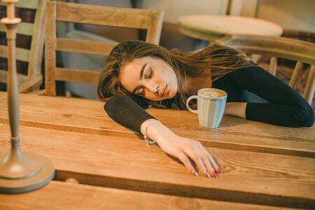 Beautiful elegant brunette girl wearing a black dress is relaxing in a street cafe. Advertising,fashion,commercial design.Girl in a cafe in a black dress brunette.Beautiful girl in a cafe.Tinted photoの写真素材